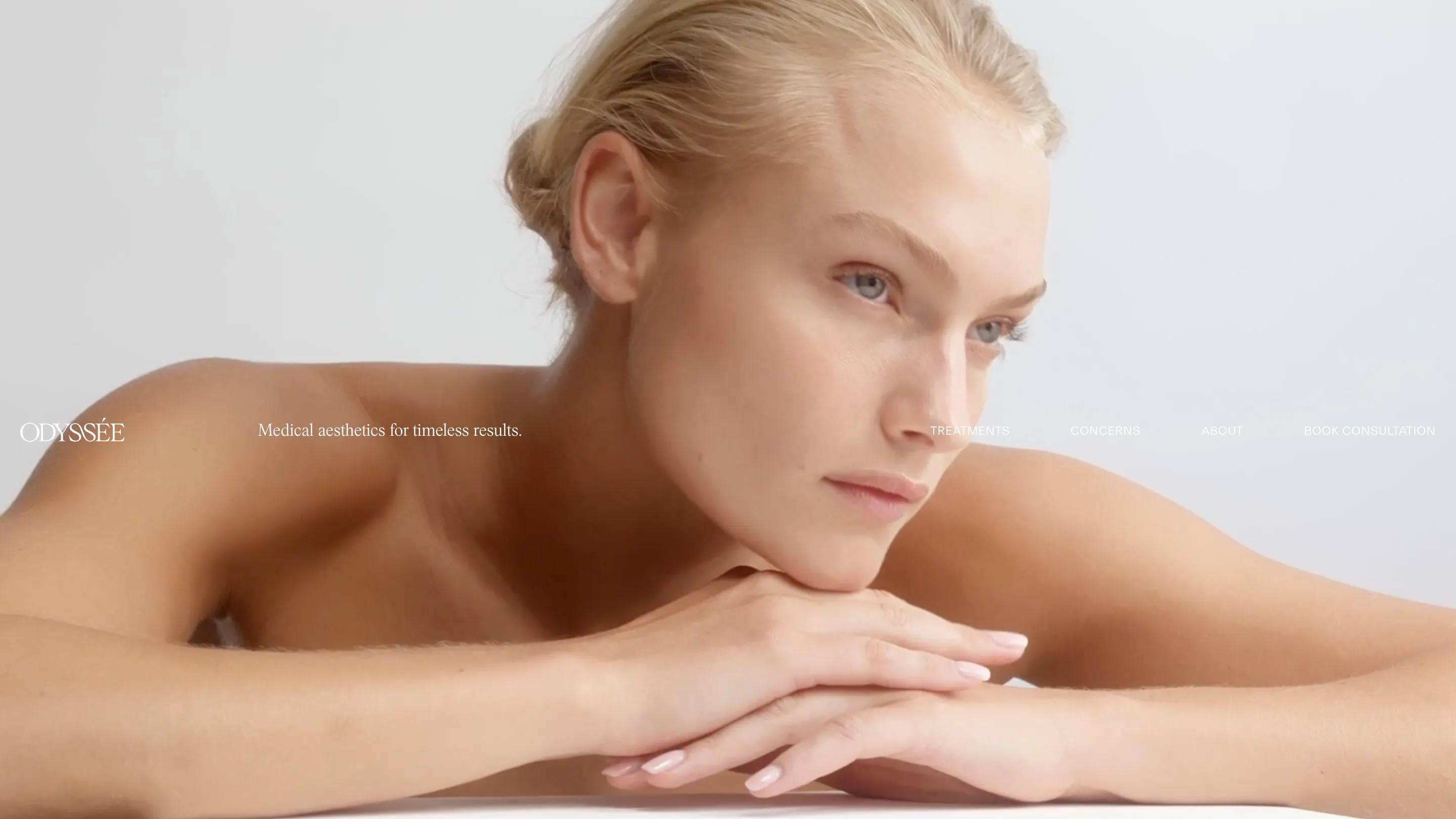 The Odyssée home page: a model resting her chin on her hands, with the wordmark, the line "Medical aesthetics for timeless results." and the nav set in one band across her shoulders