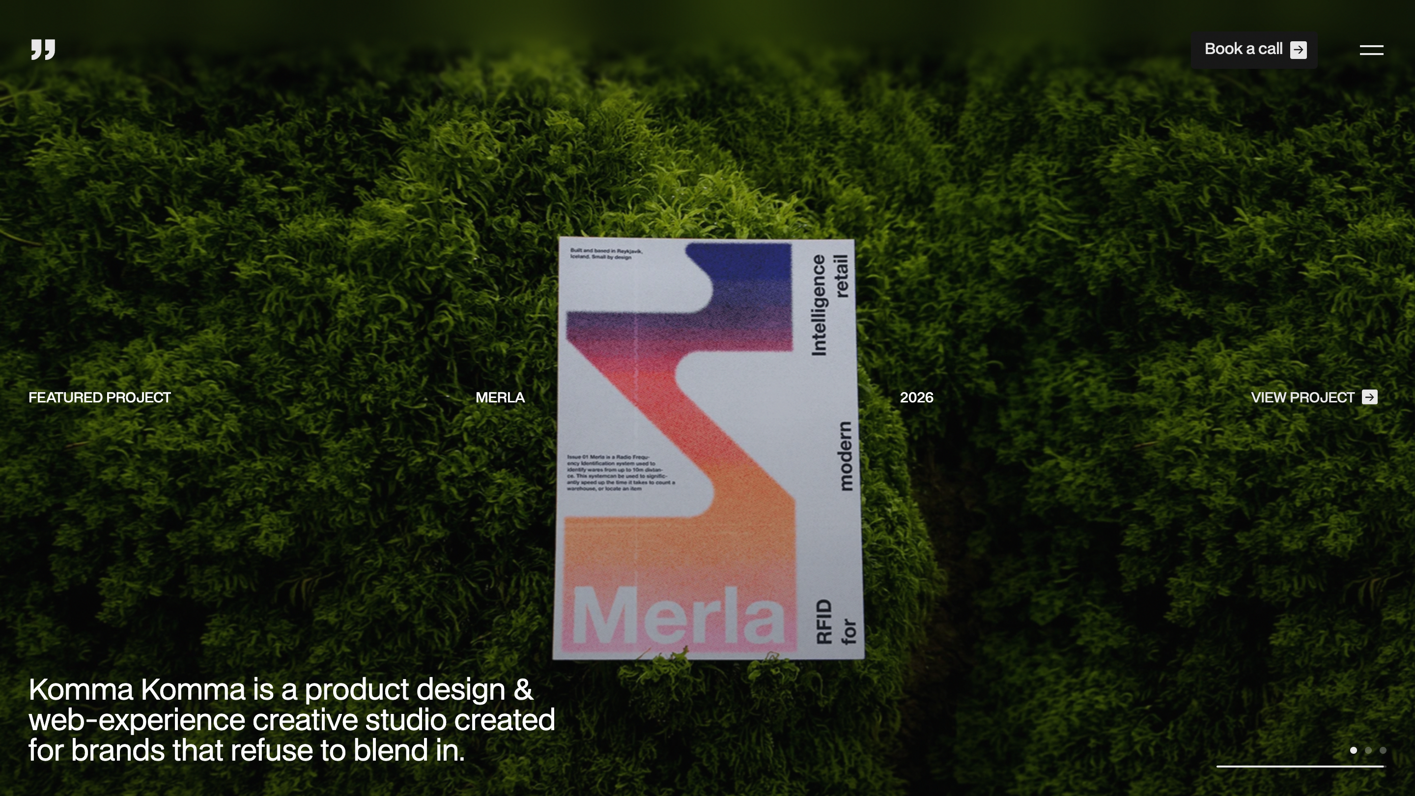 Komma Komma home page: a printed poster for the Merla project lying on green moss, with the studio tagline set in white below